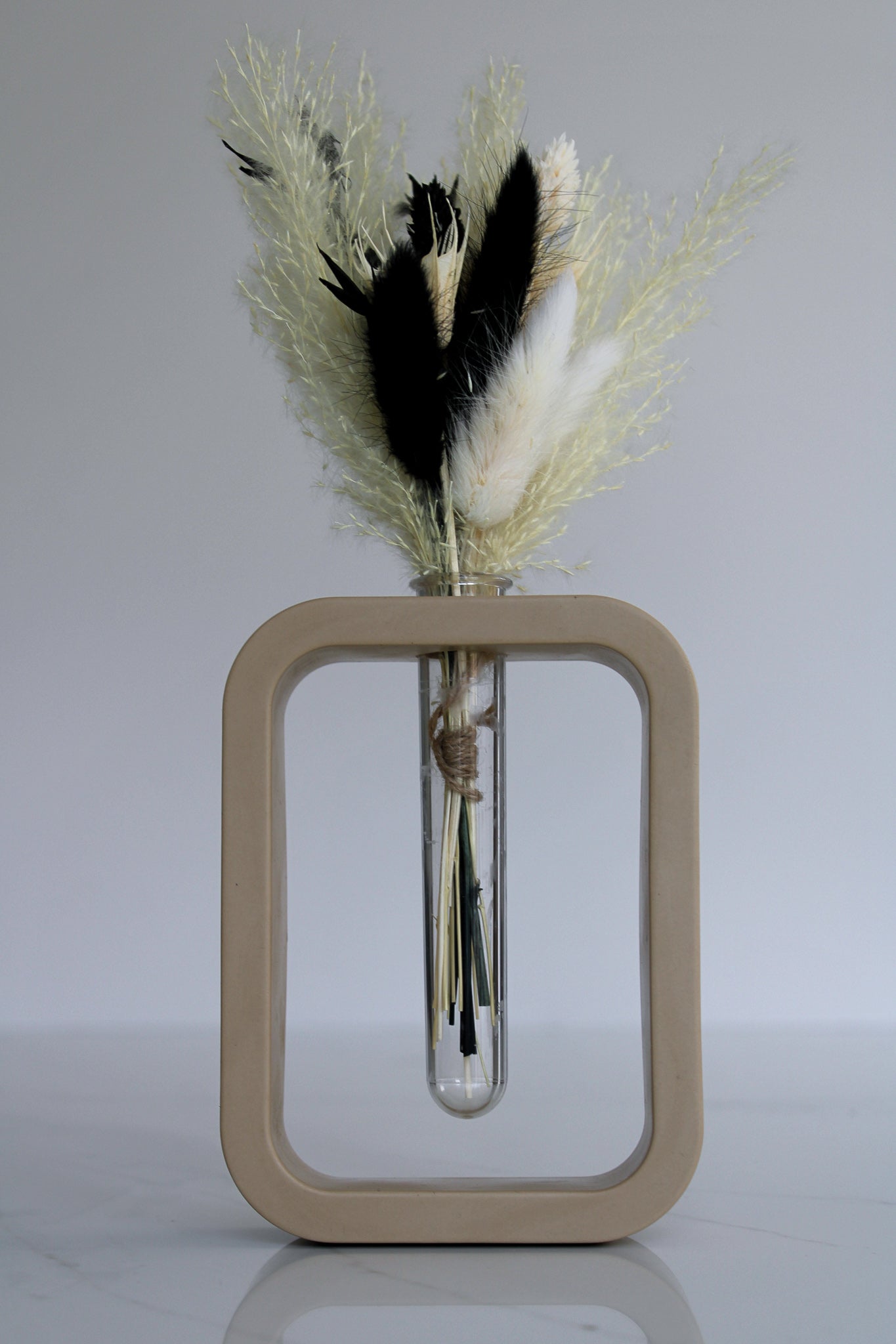 A charming beige mini vase, meticulously crafted by hand. The vase stands at a petite height, showcasing the artistry and attention to detail put into its creation. Its smooth surface boasts a warm beige finish, exuding a sense of elegance and tranquility. The compact size of the vase makes it perfect for showcasing a single delicate flower or a small floral arrangement. The organic curves and gentle contours of the vase add a touch of grace to any space, making it an exquisite addition to your home decor.