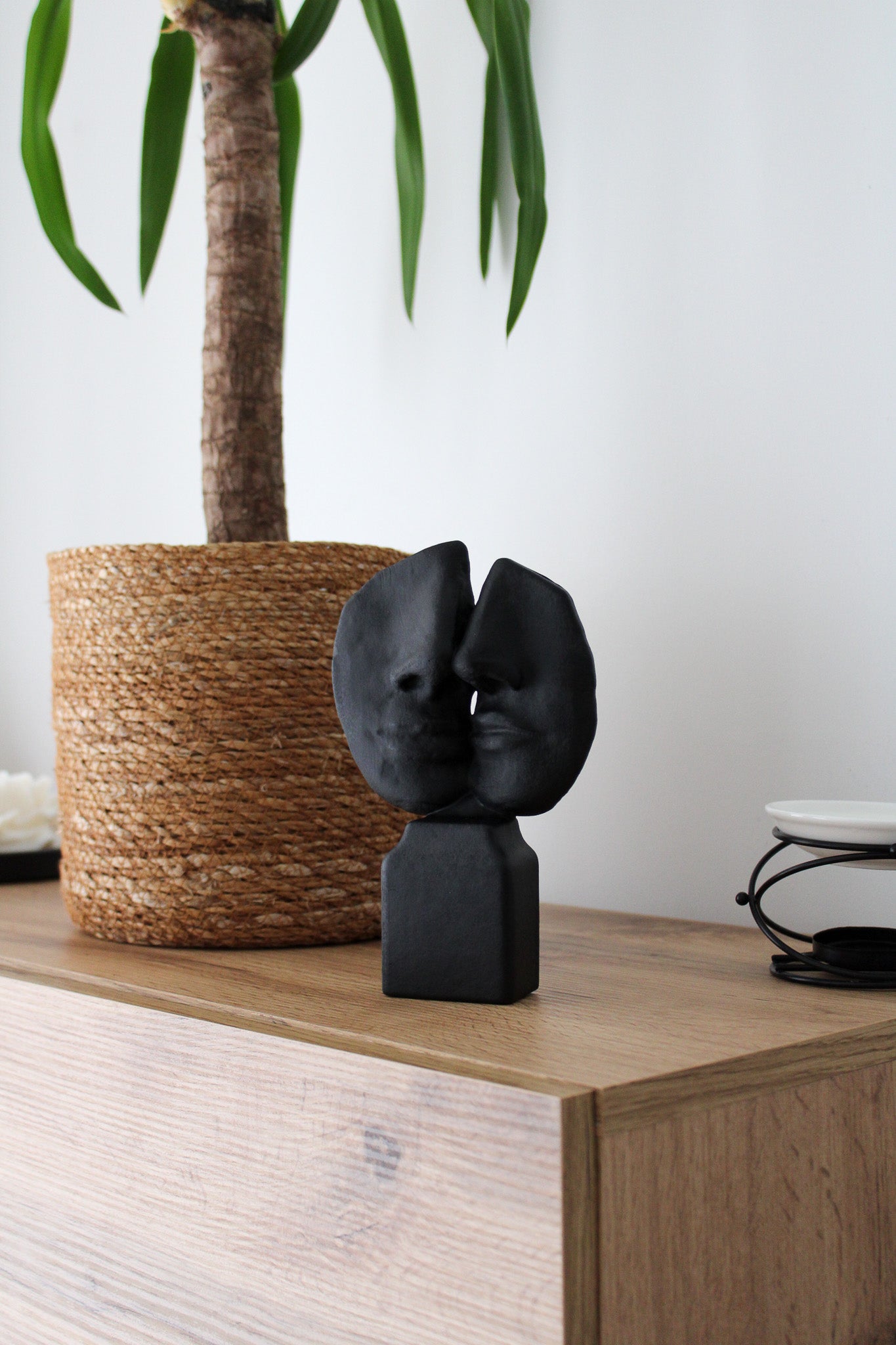 Black abstract sculpture on a wooden surface with a plant in the background