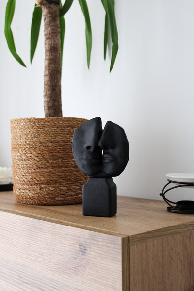 Black abstract sculpture on a wooden surface with a plant in the background